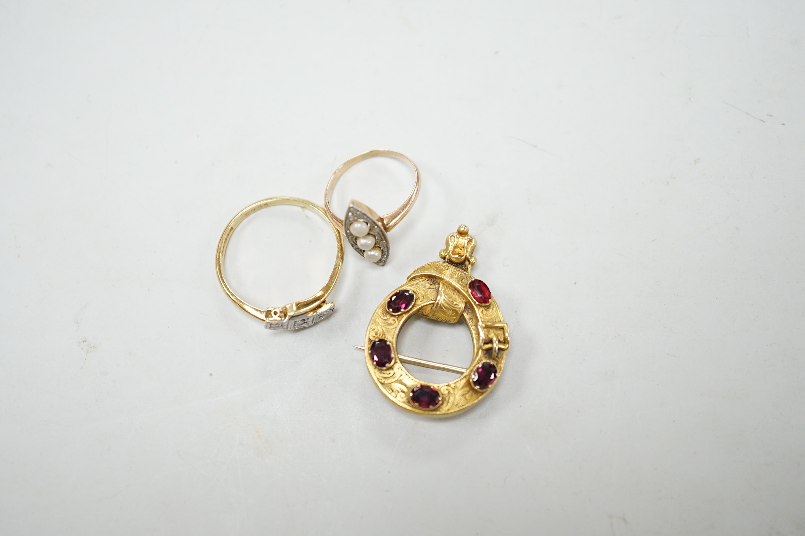 An 18c, pt and illusion set three stone diamond crossover ring, size T, a 585, three stone seed pearl and diamond chip set marquise shaped ring and a Victorian yellow metal and garnet set open work 'belt with buckle' bro